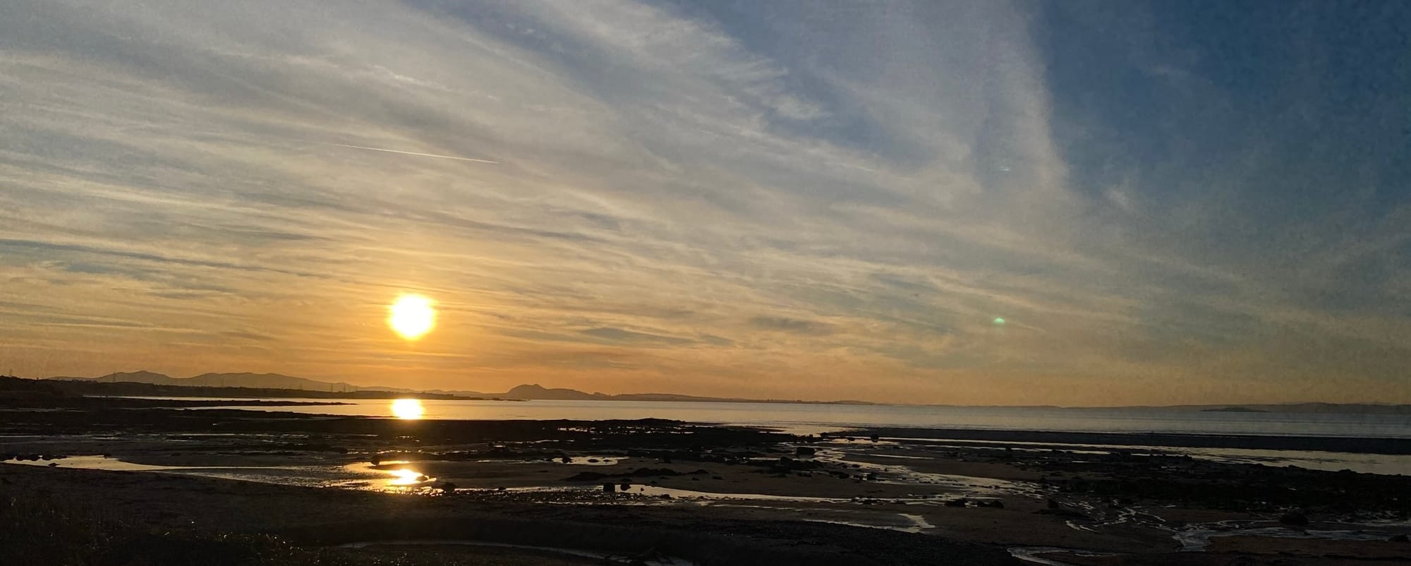 The sun setting over Edinburgh with the sea in the foreground.