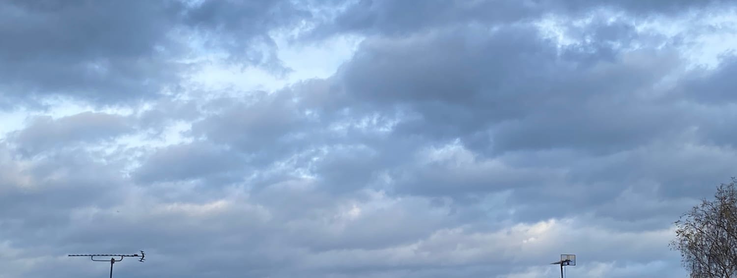 Grey clouds with slivers of blue sky, TV aerials and a tree